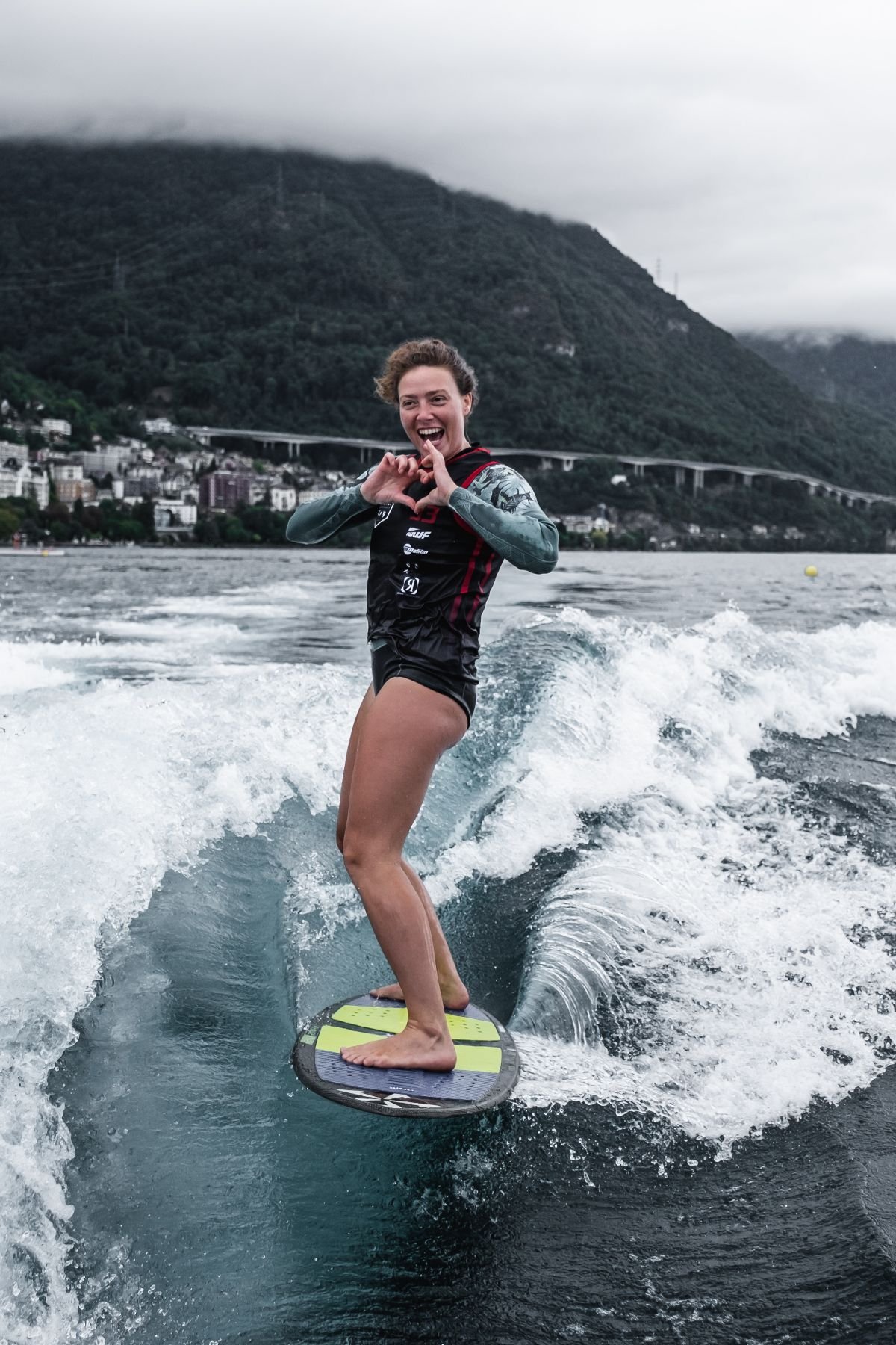 Rideuse de wakesurf souriante formant un cœur avec ses mains sur le lac Léman